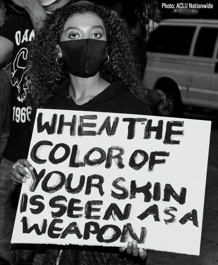 Person holding sign that says "when the color of your skin is seen as a weapon"