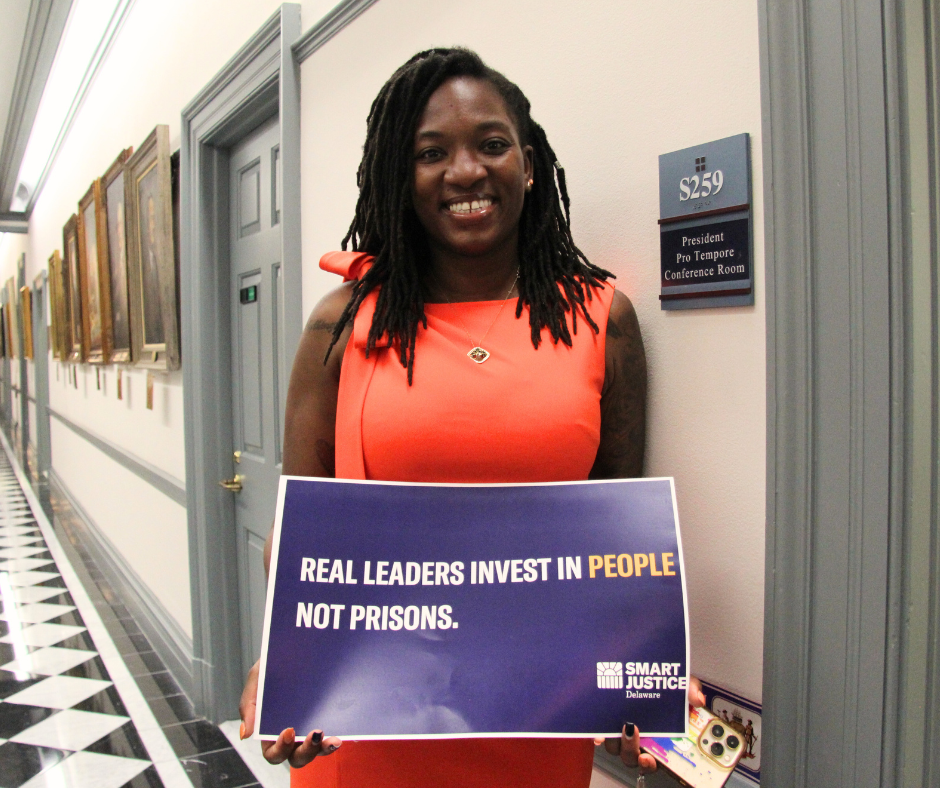 Senator Marie Pinkney holding a sign that says "Real leaders invest in people, not prisons."
